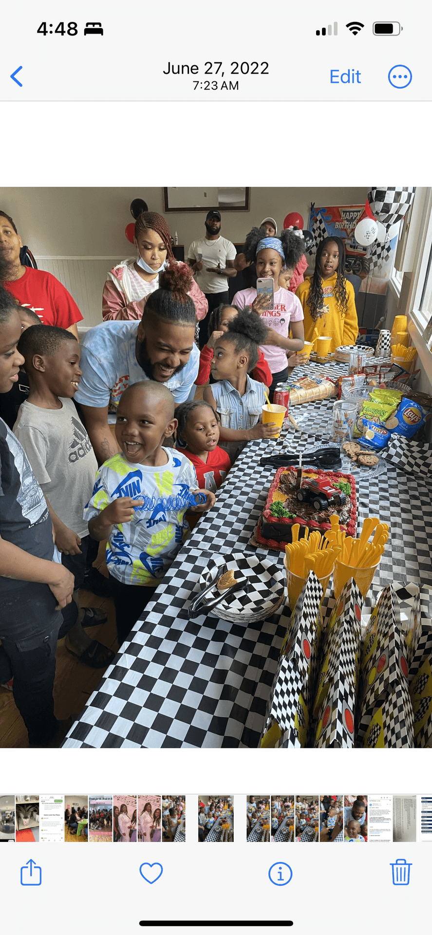 Group of children and adults gathered around a birthday table with a race car-themed cake and snacks.